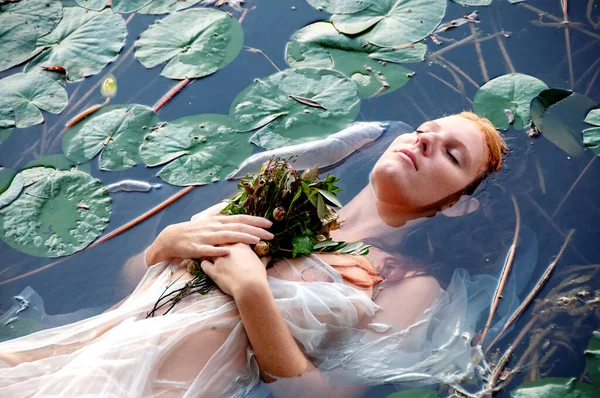 Genç ve seksi Ophelia 'nın muhteşem portresi. Kıvırcık kızıl saçlı. Huzurlu, sakin, çiçekli ve gözleri kapalı.