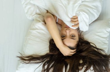 Çekici, genç, seksi, şehvetli, baştan çıkarıcı esmer kadın, uzun kahverengi saçlı, çarşafların üzerinde vahşi, Pazar sabahı, yatakta uzanıyor,