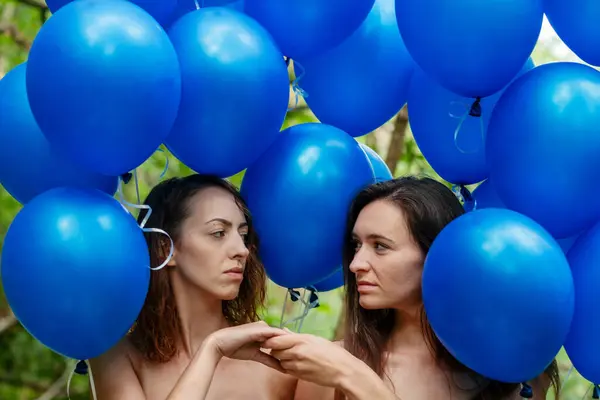 two female friends shake hands amidst blue festive balloons