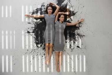 İki seksi genç kız kardeş siyah beyaz çizgili elbiseler içinde soyut siyah sanatçılar zemininde uzanan ışık ve gölge şeritleriyle biraz renk lekesiyle,