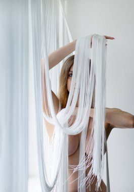 Çekici, genç, çekici, seksi, çıplak esmer kadın. Düşen bir ip perdesinin beyaz iplikleriyle kısmen gizlenmiş. Güzel şekillerde dekoratif.