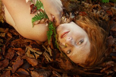 Baştan çıkarıcı genç, seksi kızıl saçlı güzel, şehvetli kadın portresi, sıcak sonbahar akşamı güneşinde, orman yaprakları üzerinde, uzay kopyaları.