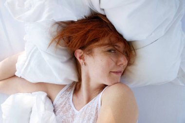 Zarif bir şekilde flört eden çekici, genç, seksi kızıl saçlı, kızıl saçlı bir kadının portresi, taze yumuşak yataktan hoşlanıyor, sabah güneşinde dinleniyor, boşluğu kopyalıyor.