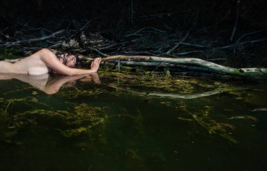 Güzel, genç, çıplak, esmer, ıslak kadın denizkızı nemli, şehvetli, hassas, yeşil, doğal su gölünde baştan çıkarıcı. Suda uzanan bir dala yapışıp kalmış.