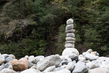 Bir yığın pürüzsüz, dengeli taş, yemyeşil bir ormanın zeminine kurulmuş kayalık bir nehir yatağında duruyor. Zen sahnesi sakinlik, denge ve doğal güzelliği çağrıştırıyor..