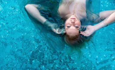 Seksi, genç, şehvetli, rüya gibi kadın turkuaz bir havuzda huzur içinde süzülüyor, gözleri yukarı bakıyor. Etrafında narin bir kumaş dolaşıyor, berrak suda ruhani ve rahatlatıcı bir atmosfer yaratıyor, uzayı kopyalıyor.