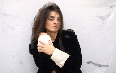 brunette woman with strands of hair gently covering her face, wearing a black velvet jacket with white cuffs. Her expression conveys introspection and melancholy against a textured wall, copy space clipart