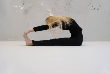 İnce sarışın kadın Paschimottanasana 'yı canlandırıyor, öne eğilmiş yoga pozu, minimalist bir stüdyoda, esneklik, odak ve sükunet sergiliyor, tarafsız bir arka plana karşı, kopyalama alanı.
