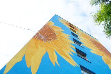 Sanatsal boyalı ev, gökyüzüne uzanan gökdelen, mavi evin duvarında, pencerelerinde, duvar resimlerinde, duvar resimlerinde, Wuppertal Oberbarmenlerinde, kopyalama alanında büyük ayçiçeği çiçekleri.