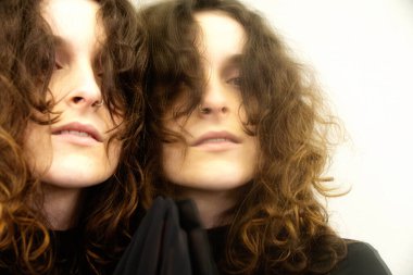 Vahşi bukleli baştan çıkarıcı, gizemli kadın aynaya bakıyor, yansıması gerçekliğe karışıyor. Yumuşak ışık ve bulanık kenarlar samimi, rüya gibi ve neredeyse gerçeküstü bir atmosfer yaratır.