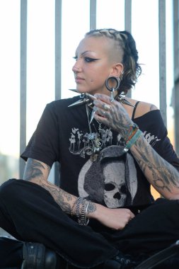 Sexy rebellious young woman with piercings, tattoos, and a bold punk gothic style sits confidently. Her edgy fashion, spiked accessories, and intense gaze exude individuality and strength, copy space clipart