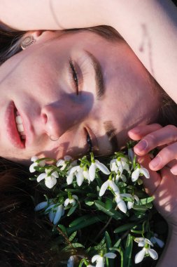 Narin kar damlalarının arasında yatan bir kadının rüya gibi, samimi bir portresi. Güneş ışığı tenini öper, yumuşak gölgeler bırakır. Dinginlik, yenilenme ve doğal güzellik anı başlıyor..