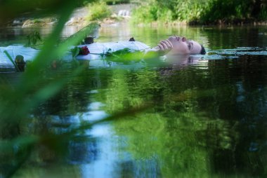 Nehirde sırtüstü yüzen kıvrımlı bir kadın, beyaz giyinmiş ve elinde güller tutuyordu, yaprakların ve suyun rüya gibi yeşil yansımalarıyla, modern bir ophelia anını anımsatıyordu..