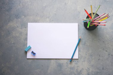 Gri arkaplanda boş kağıt, kalem, silgi ve keskinleştirici