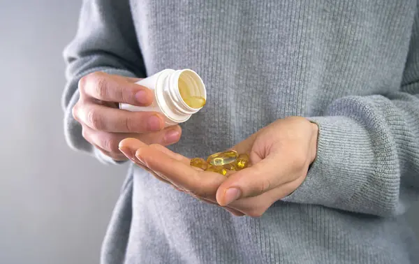 Erkek, eline balık yağı döküyor. Balık yağı kapsülleri, omega 3, omega 9, D vitamini, E vitamini.