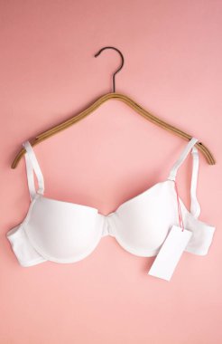 Pembe arka planda beyaz kağıt etiketli beyaz kadın sütyeni.