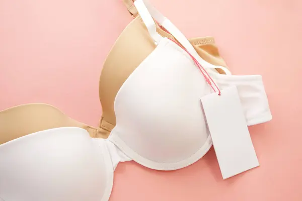 Pembe arka planda beyaz kağıt etiketli kadın sütyenleri.