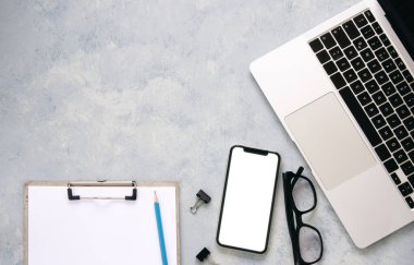 Dizüstü bilgisayarı, akıllı telefonu, gözlükleri ve diğer iş malzemeleri olan gri masa ofisi..