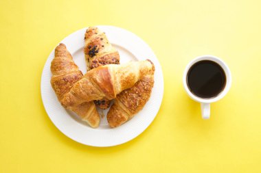 Kahve fincanı ve sarı arka planda taze kruvasanlar.
