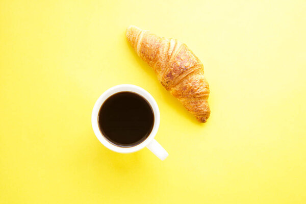 Coffee cup and fresh croissant on yellow background