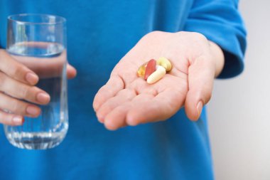 Elinde bir bardak su ve takviye kapsülü tutan kadın..