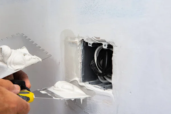 A worker repairs a wall after installing a socket box with putty