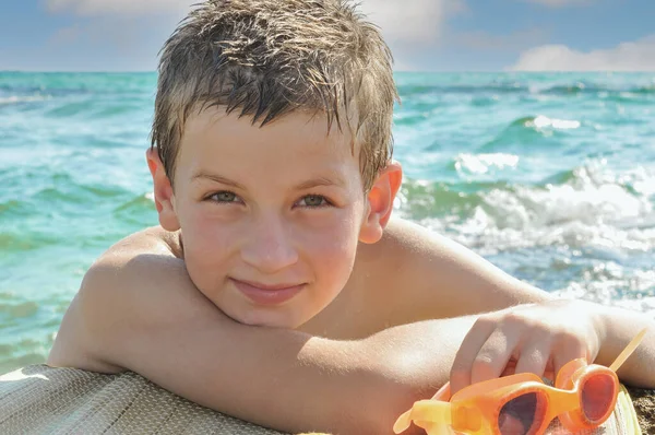 男孩游到岸边 紧紧抓住岩石 举着他的泳镜休息 图库照片
