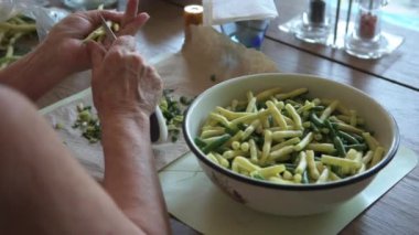 Genç sarı-yeşil fasulyeleri temizleyip kesen bir kadın.
