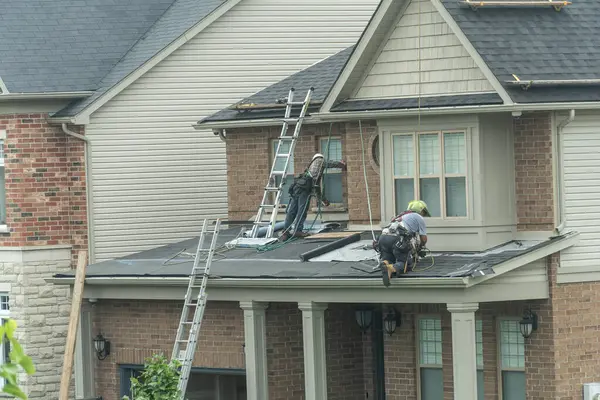 İki çatı ustası, zemin kiremitleri olan bir evin girişinin üstündeki ikinci katın çatısını tutuyorlar.