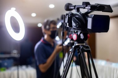 Selective focus to VDO camera with blurry cameraman working with  blurry ring lighting in studio for broadcasting. Mass media concept.