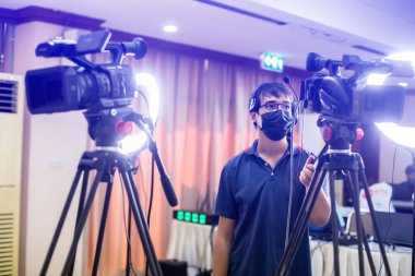 Selective focus to cameramans working with camera and blurry ring lighting in studio for broadcasting. Mass media concept.