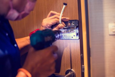 Selective focus to digital door lock pad with blurry hand of a mechanic using an electric screwdriver for installation.