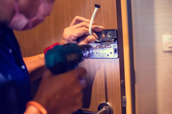 Selective focus to digital door lock pad with blurry hand of a mechanic using an electric screwdriver for installation.