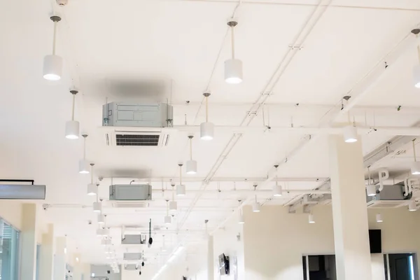 stock image Selective focus to ceiling mounted cassette type air condition units with other parts of ventilation system with hanging lights and other construction parts.