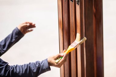 Marangozun bulanık eliyle tahtaya seçici bir odak. Yumuşak boya fırçasıyla laklak uyguluyor. El yapımı ahşap bir bankta bir fırça ile cila katmanı uygular.