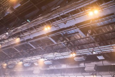 Tavana bir havalandırma sistemi, kablosuz ağ cihazları ve birçok ampulle donatılmış sıcak bir ışık yansıyor. Ticaret fuarları veya konserler için büyük toplantı odası.