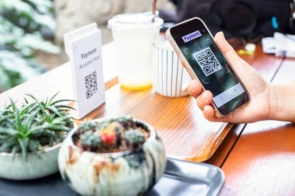 Customer hand using smart phone to scan Qr code payment tag with blur coffee on wooden table to accepted generate digital pay without money. Qr code payment concept.