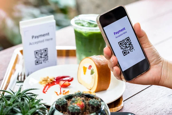 Selective focus to QR code tag on smartphone with blurry soft drink, food and  dessert in coffee shop to accepted generate digital pay without money. Qr code payment concept.