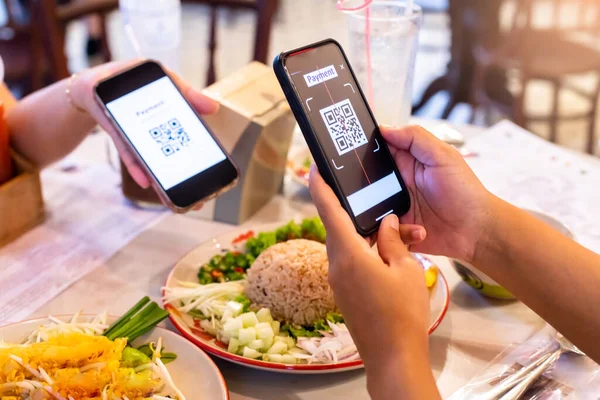 Hand using smart phone to scan QR code on tag with blurry Thai food in cafe or restaurant to accepted generate digital pay without money. Qr code payment concept.