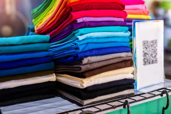 Selective focus to colorful t-shirts with blurry QR code tag in a clothing store. Payment without cash concept.