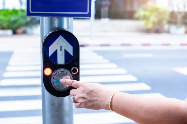 Close up pedestrian crossing call button. Hand pushing button to cross. The push button on the light pole is used when crossing a zebra crossing. Safty First.