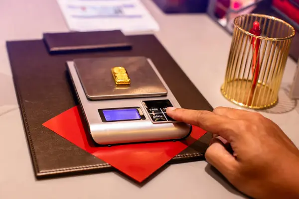 Selective focus to hand of a gold shop employee is  weighing gold bar on a digital scale. Gold trading in Thailand.