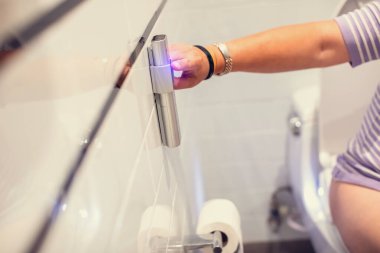 Bir kadının eli banyodaki otomatik bir klozetin uzaktan kumandasına basıyor. Tuvalette rahatlama teknolojisi..