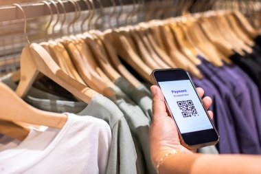 Akıllı telefondaki QR kod etiketini ödemeye seçici odaklanma ve mağazadaki birçok elbiseyi bulanıklaştırarak para olmadan dijital ödeme yapmayı kabul etmek. Qr kod ödeme kavramı.