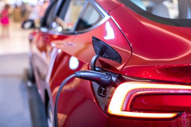 Açık hava şarj istasyonundan EV şarj pilini şarj etmek için elektrikli araca seçici odaklanma. Şarj aleti elektrik şarjı için elektrikli arabaya takıldı. EV Kırmızı Araba.