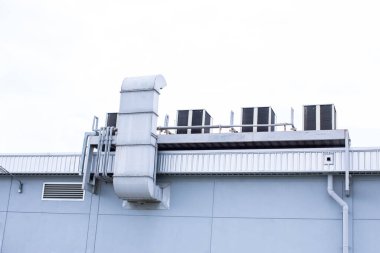 Arka planda beyaz gökyüzü olan endüstriyel bir binanın çatısında havalandırma üniteleri (HVAC). Hava kompresörü ya da hava yoğunlaştırıcı birimi çatı güvertesi binasında..