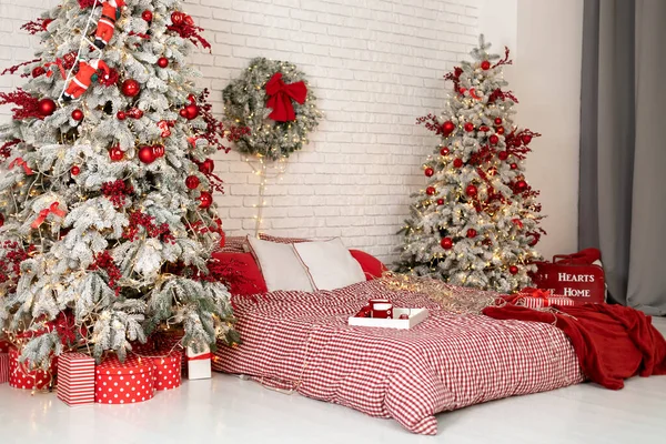  Yeni yılı ve tatilleri düşün. Kış Xmas Hygge ev dekoru. İskandinav tarzı şenlikli yatak odası. Yatağı kar kaplı iki Noel ağacı ve hediyeler..