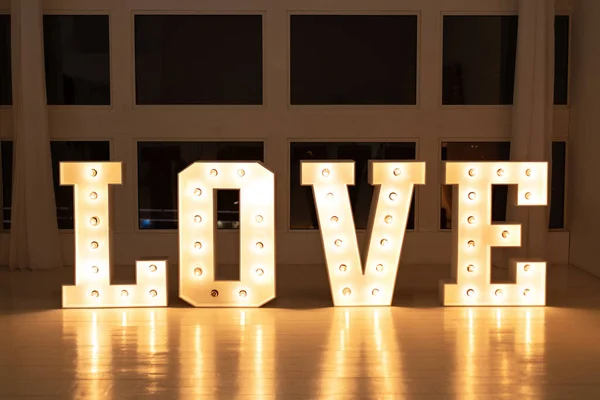 Love big white letters with led retro bulbs glowing. Word LOVE with a big letters. Inscription is love. Glowing large letters. Wedding decor. Illuminated Love sign in large letters near window.