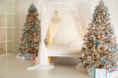 Yeni yılı ve tatilleri düşün. İç dizayn yatak odası. Kış Xmas Hygge ev dekoru. İskandinav tarzı modern beyaz yatak odası. Beyaz perdeleri ve süslü Noel ağacı olan bir yatak odası.. 