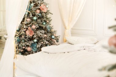 Akan beyaz perdeleri ve Noel ağacı olan modern beyaz yatak odası. Noel dekore edilmiş yatak odası iç kısmı. Beyaz çarşaflardan yapılmış bir yatak. Buruşmuş çarşafları olan dağınık bir yatağın sabah manzarası